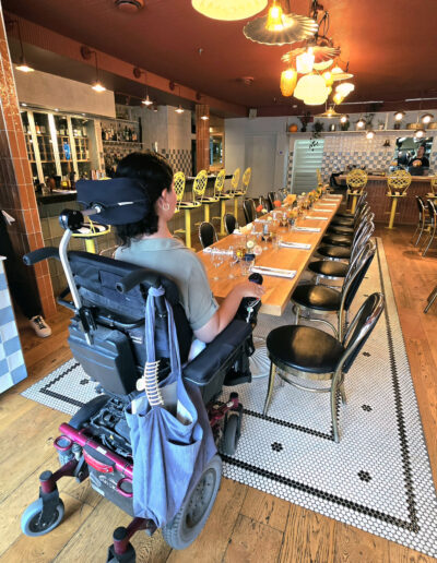 Personne en fauteuil roulant se déplaçant dans un restaurant afin de vérifier l’accessibilité des espaces et des tables.
