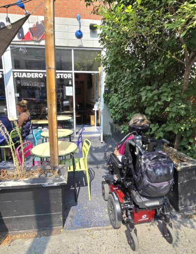 Personne en fauteuil roulant approchant l’entrée d’un restaurant avec terrasse sur l’avenue Mont-Royal à Montréal.